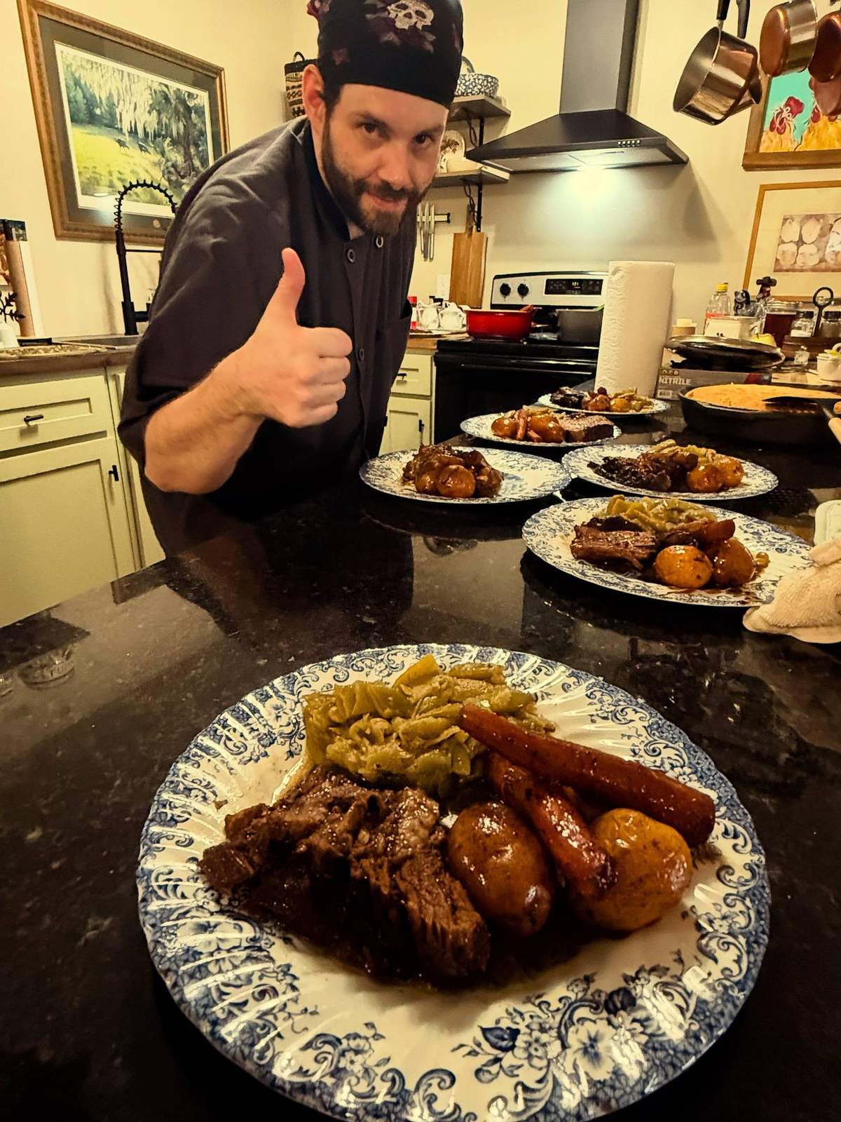 The Backcountry chef in the lodge kitchen giving a thumbs up behind plates of hand-cut steak, roasted potatoes, sausage and green beans